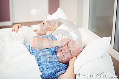 Disturbed man covering ears from snoring wife Stock Photo