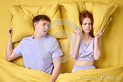 Disturbed Young Woman Covering Ears With Pillows While Man Snoring On Bed Stock Photo