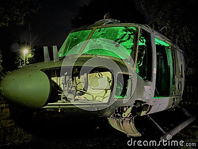 Disused abandoned Helicopter grounded at night with green lighting to show nose body component parts and lit windows Stock Photo