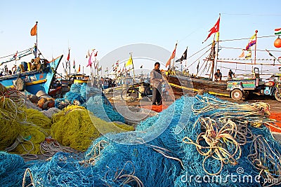 DIU, INDIA - JANUARY 9, 2014: Fisherman working on his net at Vanakbara Fishing port with colorful fishing nets in the foreground Editorial Stock Photo