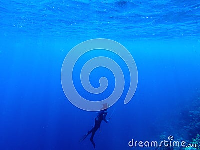 Diver underwater in deep blue sea. Man in diving gear dives up to water surface. Stock Photo