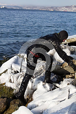 Diver working in difficult Arctic conditions. diver in black dry suit climbs on icy stones, Editorial Stock Photo