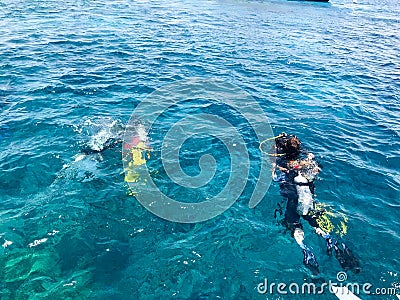 Divers in black diving waterproof suits with shiny metal aluminum canisters float, dive into the blue sea water on vacation, a sea Stock Photo