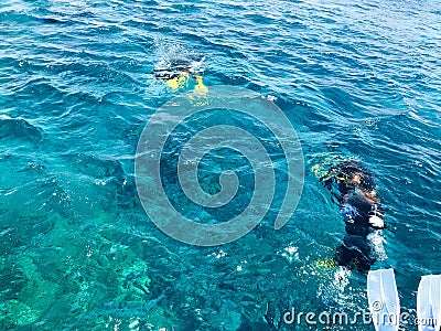 Divers in black diving waterproof suits with shiny metal aluminum canisters float, immerse in blue sea water on vacation, a sea cr Stock Photo