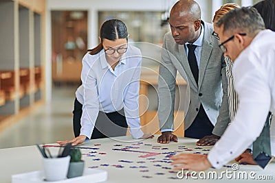 Diverse businesspeople solving a jigsaw puzzle together at work Stock Photo