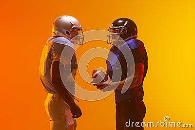 Diverse male american football players holding ball with neon orange lighting Stock Photo
