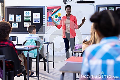 Diverse pupils sitting at desks listening to female teacher at front of class Stock Photo