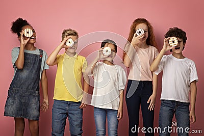 Diverse schoolkids holding yummy donuts in front of their faces over pink background Stock Photo