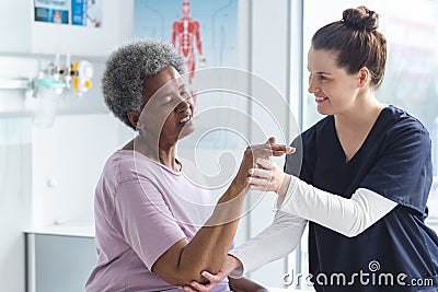 Diverse senior female patient exercising hand and female doctor advising in hospital room Stock Photo
