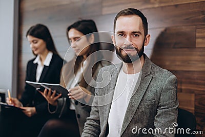 Diverse young businesspeople students friends sitting together in chairs in queue using mobile phones wait job interview or Stock Photo