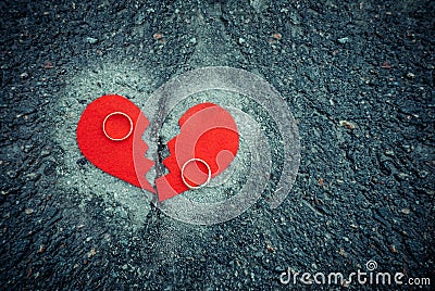 Divorce concept - broken heart with wedding rings on cracked asphalt. Toned Stock Photo