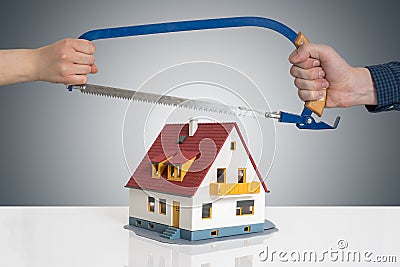 Divorce and dividing a house concept. Man and woman are splitting model of house with saw Stock Photo