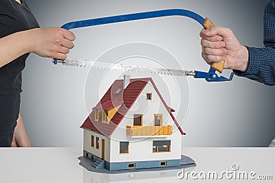 Divorce and dividing a house concept. Man and woman are splitting model of house with saw Stock Photo