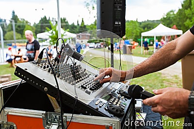 DJ is adjusting the levels on his mixing board during a community event Stock Photo