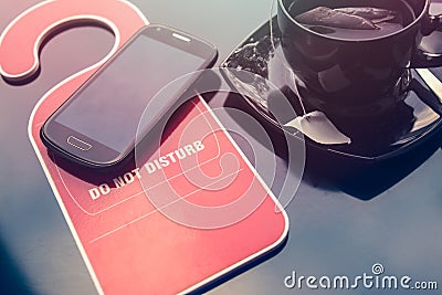 Do not disturbe sign, a cup of tea and a mobile phone over dark background. Time for rest concept. Stock Photo