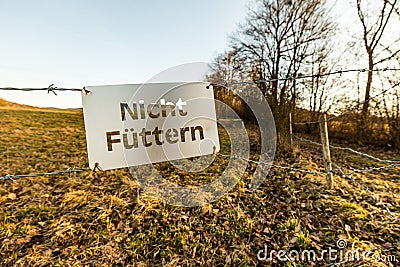 `Do not feed` sign written in german nicht fÃ¼ttern hanging on a barbwire at a fields for horses and donkeys Stock Photo