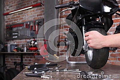 Do it yourself, hands repairing a motorcycle in the garage with red brick wall, pegboard work tools and wrenches in the work bench Stock Photo