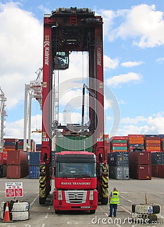Dock straddle carrier loading a shipping container onto a trailer being pulled by a red Renault Magnum truck Editorial Stock Photo