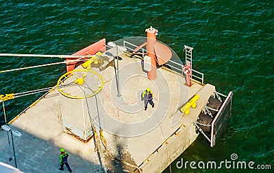 Dockworkers attaching moored ship`s hawser to shoreside bitt in seaport`s dock Editorial Stock Photo