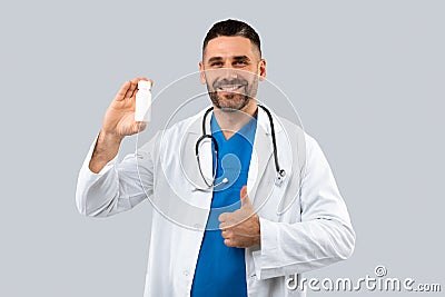 Doctor advice. Happy middle aged man therapist in white coat showing jar of pills and gesturing thumb up Stock Photo