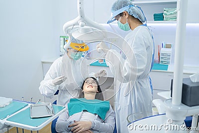 Doctor and assistance in protective masks serving Asian young woman patient by examining teeth or dental checkup at dental clinic. Stock Photo