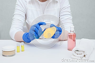 The doctor beautician in gloves and mask holds a bottle and cosmetic sponge in his hands Stock Photo