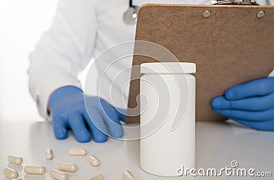 Doctor with blue gloves and clipboard and pills laying on table. Stock Photo