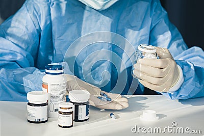 Doctor in a blue surgical gown and mask holds in his hand a medicine bottle. Many pills and drugs on white table, healthcare Stock Photo