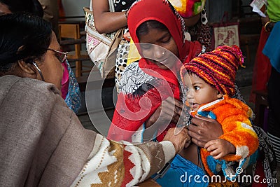 A doctor is checking a lovely little boy sitting on her mothers lap. Editorial Stock Photo