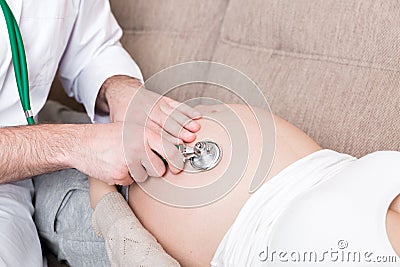 Doctor is checking pregnant woman`s belly with a stethoscope. Physician is listening to a heartbeat of a baby Stock Photo
