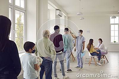 Doctor checks temperature with a non-contact infrared thermometer in people who came for vaccination. Stock Photo