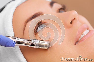 The doctor-cosmetologist makes the procedure Microdermabrasion of the facial skin of a beautiful, young woman in a beauty salon. Stock Photo