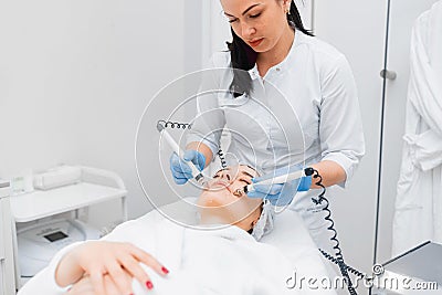 The doctor in the cosmetology office makes a young beautiful girl a microcurrent facial massage Stock Photo