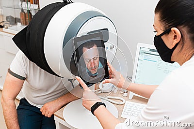The doctor diagnoses the condition of the skin of the man`s face using modern cosmetic equipment Stock Photo