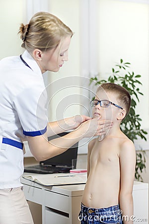 Doctor in a doctor`s office while medical examining the tonsils of a boy with glasses. Stock Photo