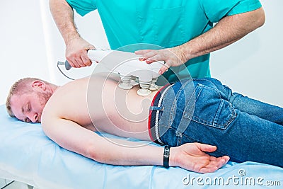 Doctor does transcranial magnetic stimulation, electrotherapeutic treatment of the back. A chiropractor treats patient`s loins Stock Photo