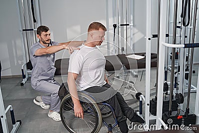 Doctor examines wheelchair man posture in rehab center gym Stock Photo