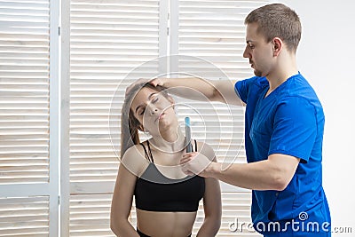 The doctor gives a neck massage with a special medical stick to a young girl Stock Photo