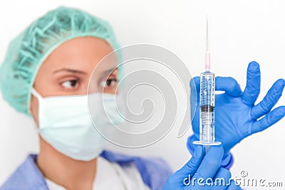 A doctor with gloves and face msk holds a syringe Stock Photo