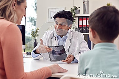 Doctor Or GP In White Coat Meeting Mother And Son For Appointment Looking At Scan On Digital Tablet Stock Photo