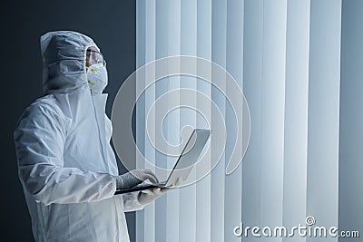 Doctor in hazmat suit works with laptop Stock Photo