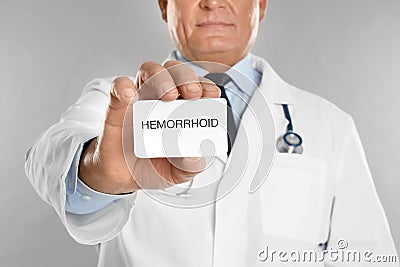 Doctor holding business card with word HEMORRHOID on light grey background, closeup Stock Photo