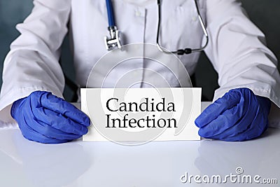 Doctor holding card with phrase Candida Infection at white table, closeup Stock Photo