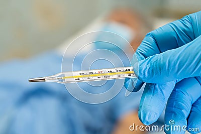 Doctor holding digital thermometer to measures asian senior or elderly old lady woman patient wearing a face mask have a fever Stock Photo