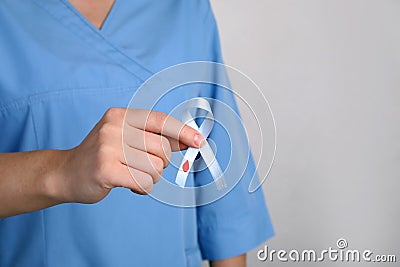 Doctor holding light blue ribbon with paper blood drop on grey background, closeup. World Diabetes Day Stock Photo