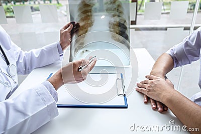 Doctor holding and looking at x-ray film examining at lungs radiograph of patient chest injury and analyze result while discussing Stock Photo