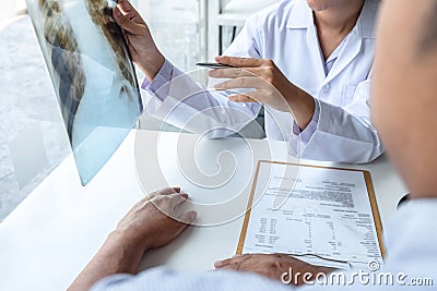 Doctor holding and looking at x-ray film examining at lungs radiograph of patient chest injury and analyze result while discussing Stock Photo
