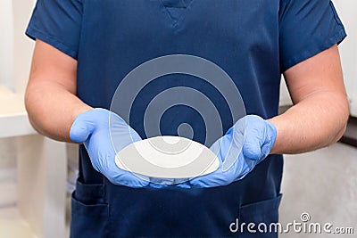 Doctor holding silicone implant for breast augmentation, space for text. Plastic surgeon hands holding silicon breast implants. Stock Photo