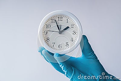 Doctor holding white alarm clock in hand with glove Stock Photo