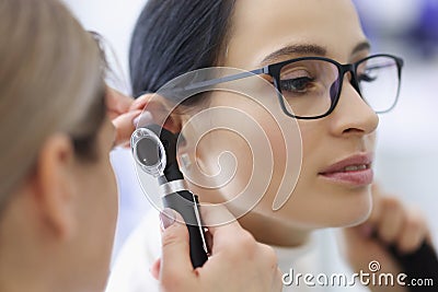 Doctor laryngologist examining ear of female patient with glasses using otoscope Stock Photo